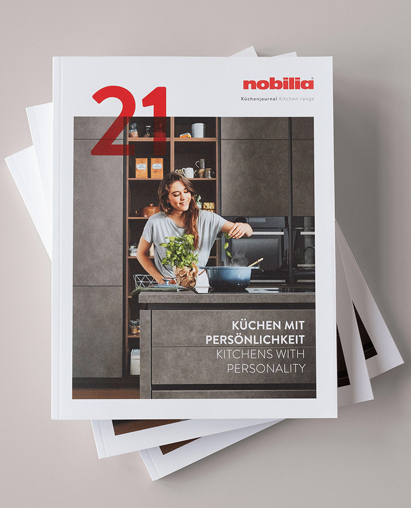 Nobilia Titel Küchenjournal, junge Frau kocht in moderner Küche in Betonoptik, Überschrift Küchen mit Persönlichkeit